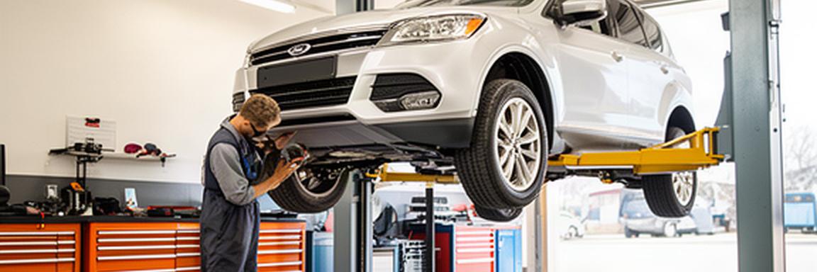Mechanic inspecting a silver vehicle on a lift inside a clean automotive service bay
