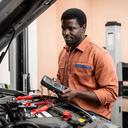 Automotive technician Daniel Okafor testing a vehicle battery beside a service lift